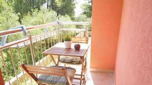 Een balkon met een tafel, stoelen, een bloempot en uitzicht op groen.