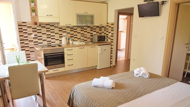 Een compacte hotelkamer met kitchenette, een bed met handdoeken en een aan de muur bevestigde televisie.