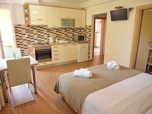 Een compacte hotelkamer met kitchenette, een bed met handdoeken en een aan de muur bevestigde televisie.