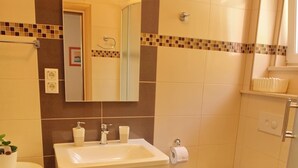 Een badkamer met een wastafel, spiegel, toilet en een klein plankje met toiletartikelen.