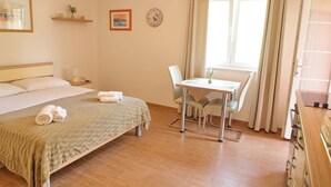 Hotelkamer met een bed, een klein tafeltje met stoelen, een raam met gordijnen, een klok en een plank met decoratieve spullen.