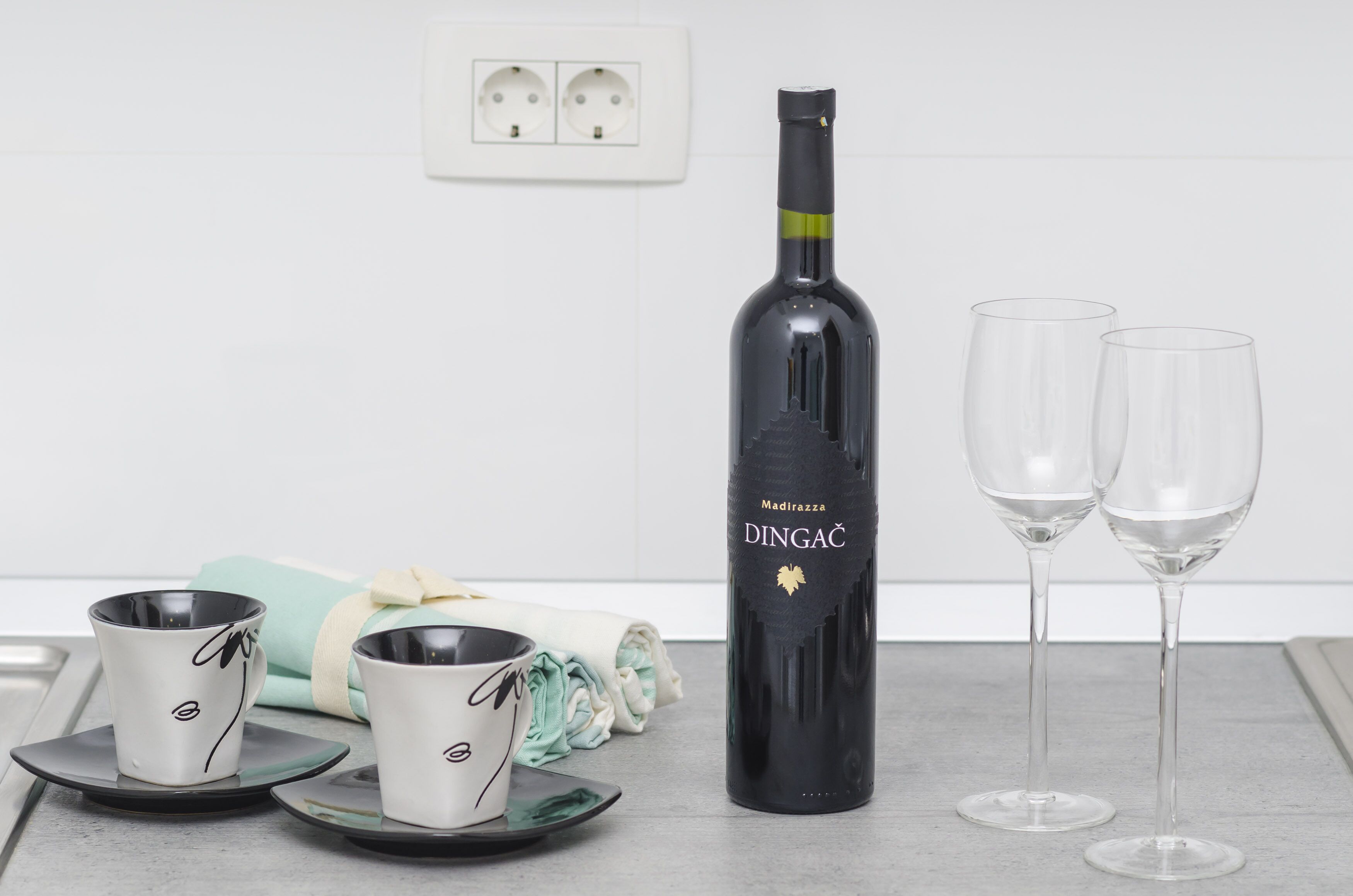 A bottle of wine, two glasses, and two cups on a table.