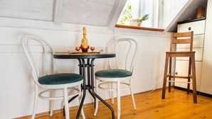 Una habitación acogedora con piso de madera, una mesita con dos sillas, un tapete de cuero y una ventana con una planta.