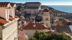 Un pueblo costero con edificios históricos, una iglesia destacada con cúpula y un muro fortificado con vista al mar.