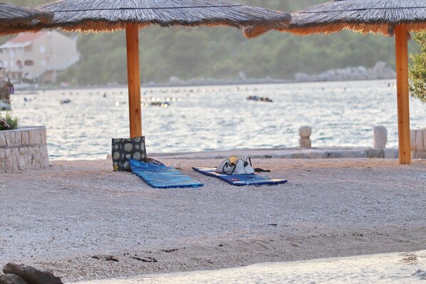 Una playa con sombrillas y sillas de descanso, un muro de piedra y vistas al mar.
