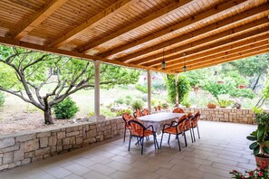 Eine überdachte Terrasse mit einer Steinwand, Holzboden und einem Tisch mit Stühlen.