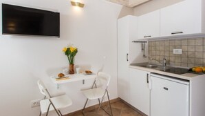 Une cuisine compacte avec des meubles blancs, un four encastré, un évier et un téléviseur à écran plat fixé au mur.