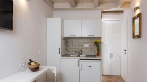 Une cuisine compacte avec des meubles blancs, un pare-feu en carrelage, un petit réfrigérateur et un coin repas comprenant une table et des chaises blanches.