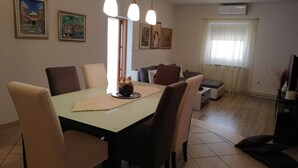 A dining area with a table, chairs, and hanging pendant lights. There are framed artworks on the walls and a window with curtains.