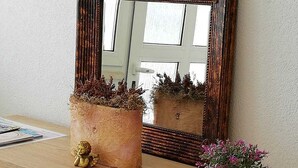 A wooden dresser with a mirror, two potted plants, and a small golden statue.