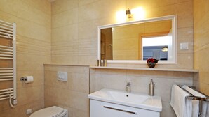 A bathroom with a toilet, sink, mirror, towel rack, and a wall-mounted heater.