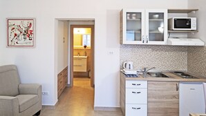A compact kitchen with a microwave, sink, and cabinet. A sofa and a bed are visible in the adjacent living area.