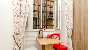 Une petite pièce avec une table en bois, deux chaises, une fenêtre avec des barreaux en métal et une chaise rouge.