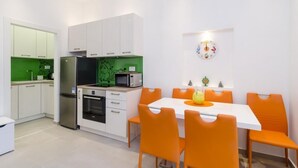 Eine moderne Küche mit weißen Schränken, einer grünen Spritzschutzleiste und einem Essbereich mit orangefarbenen Stühlen und einem weißen Tisch.