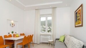 Ein modernes Wohnzimmer mit Essbereich, einem großen Fenster mit Vorhängen, einem grauen Sofa und einem Gemälde an der Wand.
