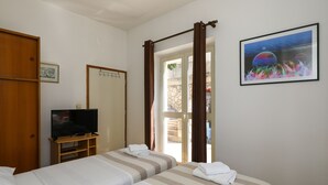 Ein Hotelzimmer mit zwei Betten, einem Fernseher auf einem Holzständer, einem Bild an der Wand und einer Tür zu einem Außenbereich.