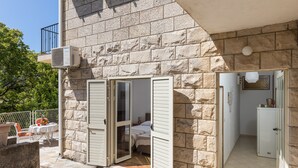 Ein Steinhaus mit Balkon, ein kleines Zimmer mit Bett und einer Küchenzeile.
