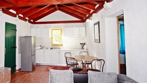 A compact kitchen with white cabinets, a stainless steel refrigerator, and a dining area with a wooden table and metal chairs. - Holiday Home Harmony - Holiday Home with Terrace (Dol)