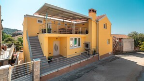 A two-story yellow building with a balcony, a staircase, and a chimney.