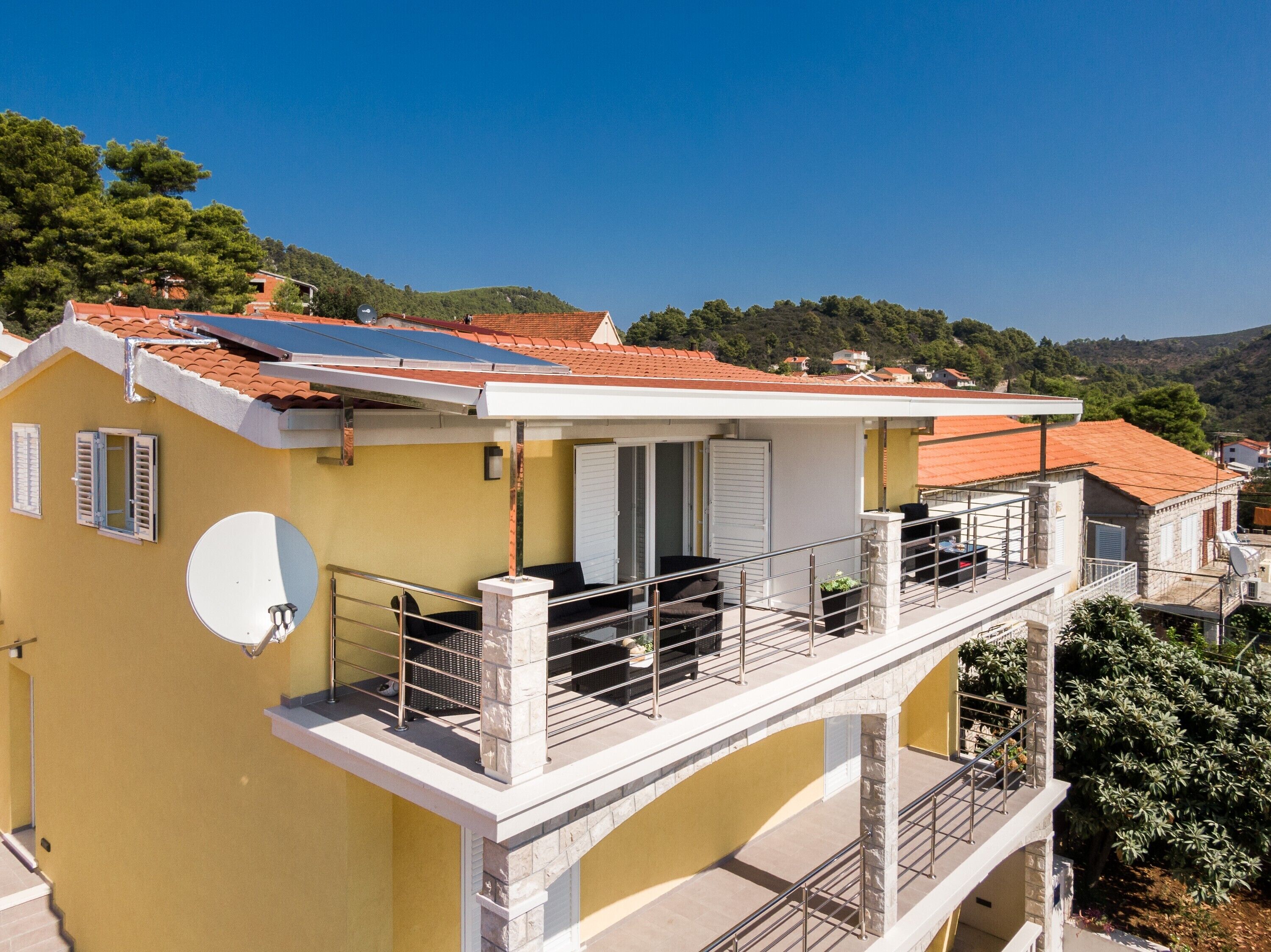Een geel gebouw met een balkon, zonnepanelen en een satellietschotel.