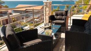A balcony with wicker furniture, a glass table, and a bottle of wine.