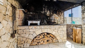 An outdoor stone fireplace with a brick oven, logs, and cooking utensils. - Apartments & Rooms Cina - Studio Apartment with Sea View (Cavtat)