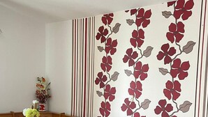 Een woonkamer met een beige bank, een houten eettafel met stoelen en een wanddecoratie met rode en witte bloemen.