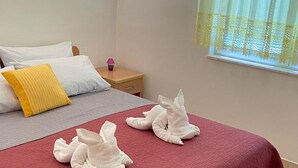 Een netjes opgemaakt bed met een rode spreideken, twee kussens en twee handdoeken gevouwen in de vorm van een zwaan.