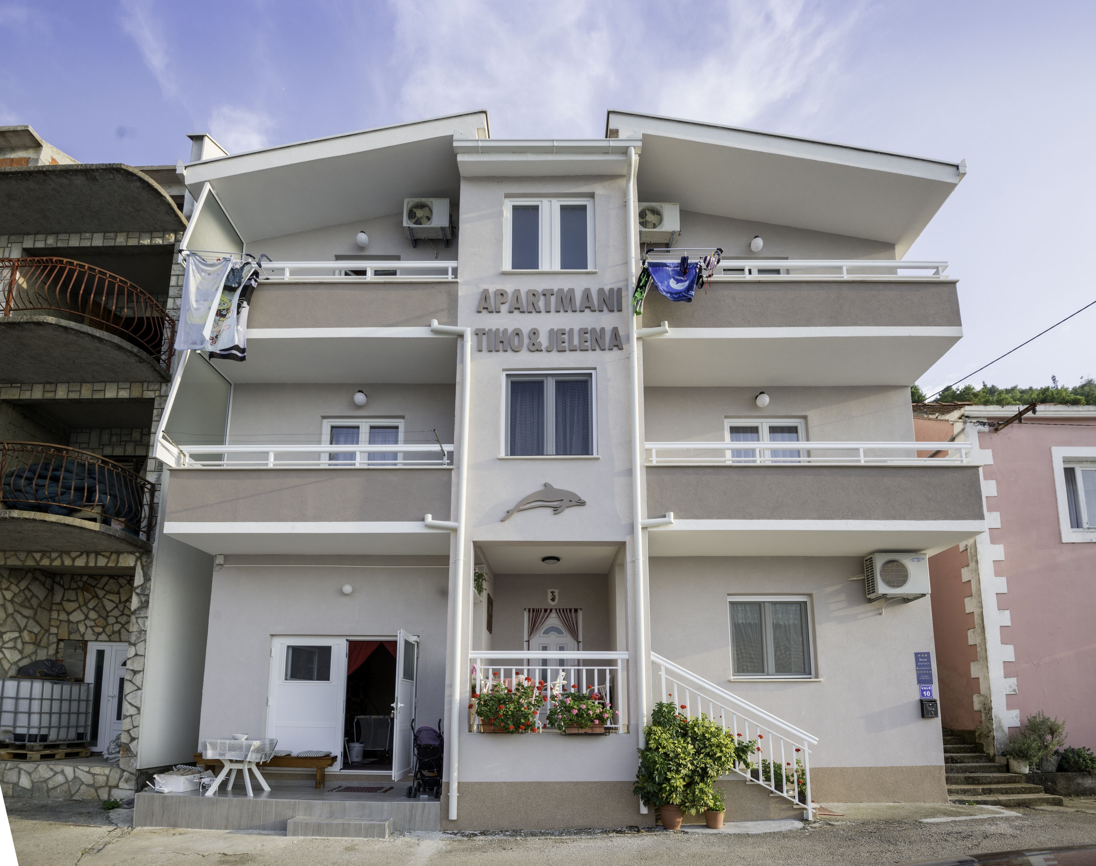 A multi-story apartment building with balconies, a staircase, and a sign that reads "APARTMANTI TIOHO & JELENA".