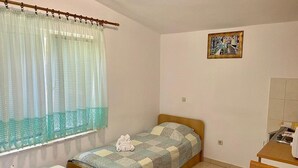 Ein kleines Schlafzimmer mit zwei Einzelbetten, einem Holz-Kopfteil, einem kleinen Tisch und einem Fenster mit durchsichtigen Vorhängen.