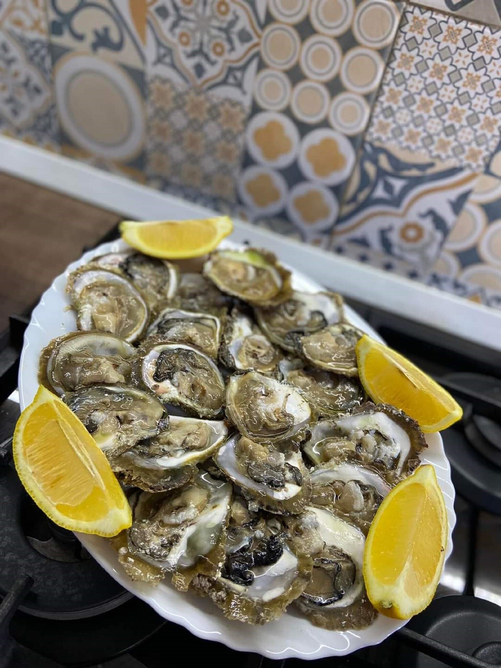Un plato de ostras con gajos de limón sobre un plato blanco.