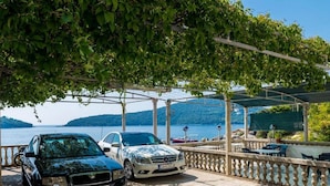 A covered parking area with two cars parked under a pergola, overlooking a body of water and hills. - Apartments Rašica Molunat - One Bedroom Apartment (Molunat)