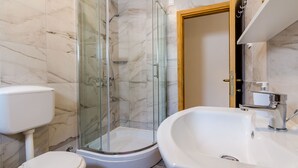 A bathroom with a glass-enclosed shower, a toilet, and a sink.
