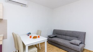 A compact living space with a white table, two chairs, a grey sofa, and a small dining table with a plate and drinks.