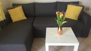 A sectional sofa with two yellow pillows, a white coffee table, and a vase with flowers. - Apartments Roko (ST) - Economy One Bedroom Apartment with Shared Terrace (A2) (Split)