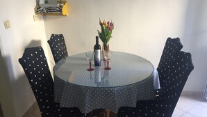 A round glass table with a polka dot tablecloth, surrounded by four chairs with similar polka dot upholstery. A bottle and a glass are on the table, and a vase with flowers is also present. - Apartments Roko (ST) - Economy One Bedroom Apartment with Shared Terrace (A2) (Split)