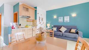 Eine moderne Küche mit Holzschränken, einem Esstisch mit Stühlen und einem Wohnbereich mit einer Couch und Wandbildern.
