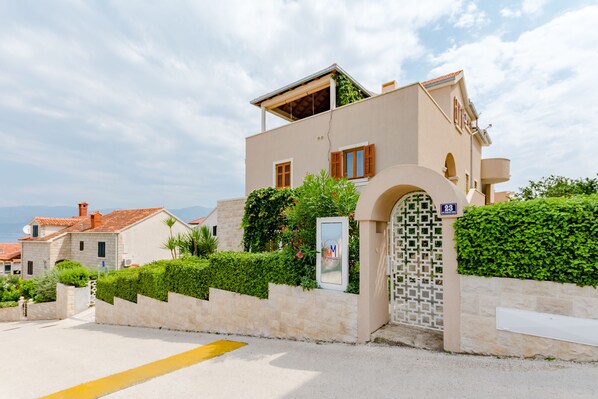 Un bâtiment à deux étages, doté d’une façade beige, d’une entrée bien visible avec un portail décoratif et d’un petit balcon à l’étage supérieur.