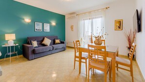 Ein Wohnzimmer mit türkisfarbenen Wänden, einem grauen Sofa, einem Esstisch mit Holzkästen und einem kleinen Beistelltisch mit Lampe.