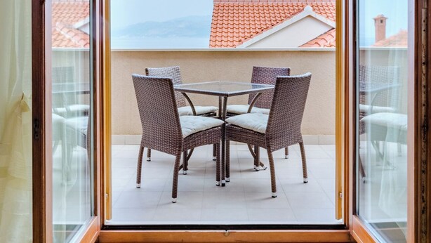 Ein Balkon mit Tisch und Stühlen, Blick auf ein rotes Ziegeldach und einen klaren Himmel.