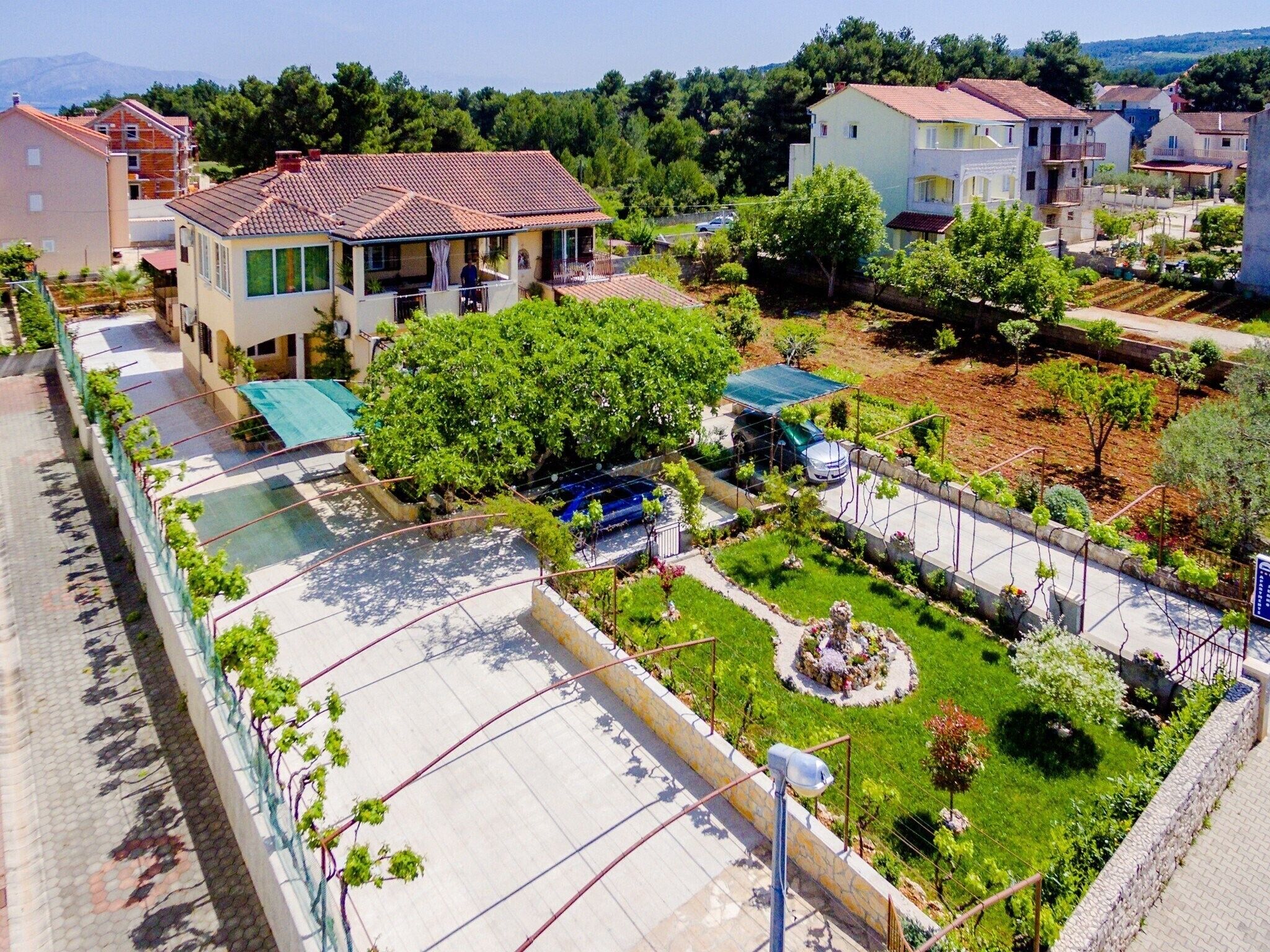 A residential area with a house featuring a tiled roof, a garden with a fountain, and a paved driveway.