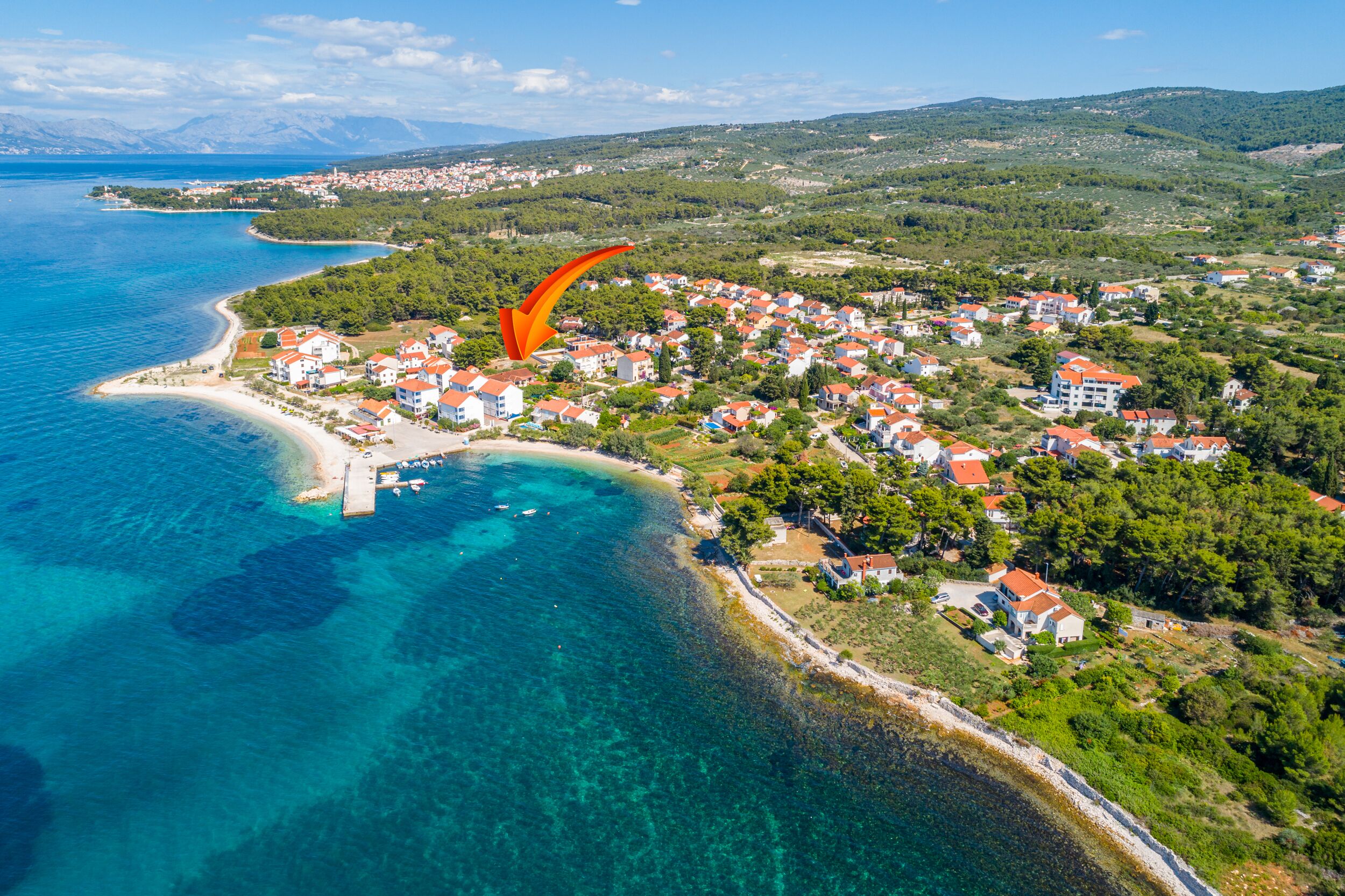 An aerial view of a coastal town with a beach, houses, and a mountainous backdrop.