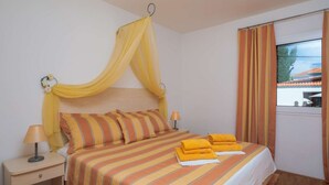 A neatly made bed with striped bedding, a bedside lamp, and a window with curtains.