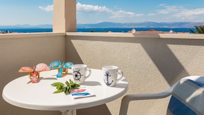 A small round table with a white mug, a blue mug with an anchor design, a colorful umbrella, and a small plant.