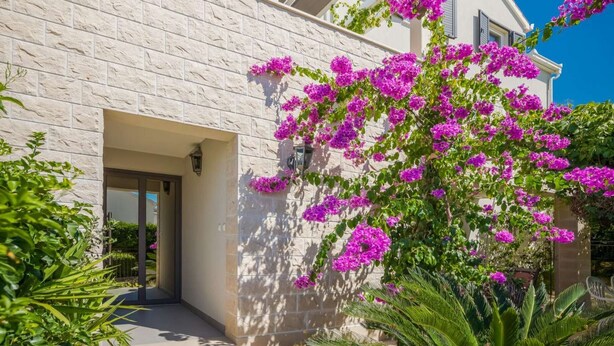 A modern building with a stone facade and a balcony with purple flowers.