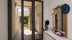 A modern interior with a sliding glass door leading to a balcony, a white console table with decorative items, and a mirror with hats hanging on the wall.