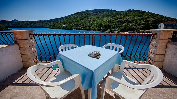 Un balcone con tavolo e sedie, affaccia su un corpo d'acqua e una collina.
