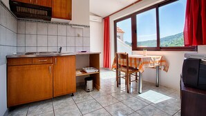 Una cucina compatta con mobili in legno, zoccolo piastrellato, una finestra con tende rosse e un'area pranzo con tavolo e sedie.