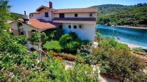 Una casa a due piani con tetto in tegole rosse, circondata da vegetazione lussureggiante e da uno specchio d'acqua.