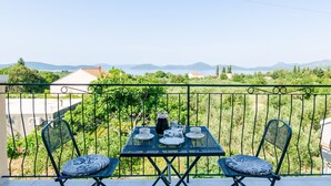Un balcon avec une table dressée pour deux personnes, offrant une vue panoramique sur un paysage magnifique, avec des montagnes et une végétation luxuriante.